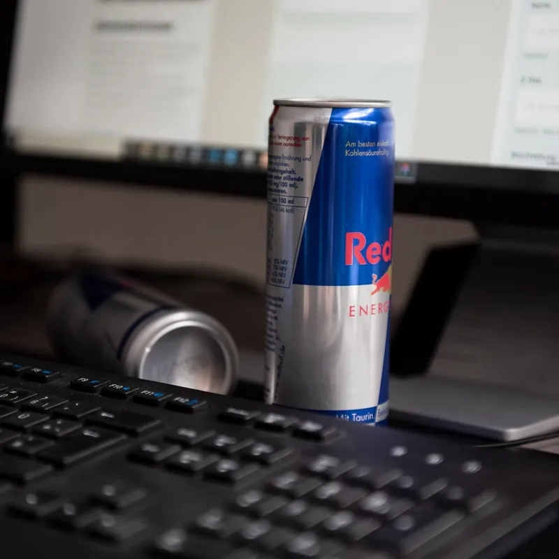 Eine Dose Redbull hinter einer Tastatur und vor einem Bildschirm